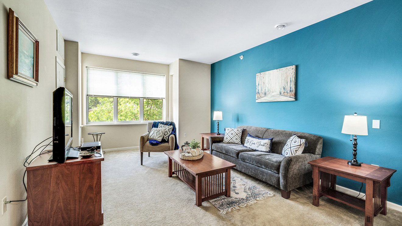 Bright senior apartment with accent wall, sofa and TV where residents can retreat to read or enjoy entertainment with friends at Holiday Village at the Falls.